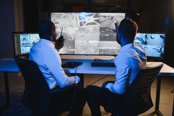 In the Security Control Room Two Officers Monitoring Multiple Screens for Suspicious Activities, They Report any Unauthorised Activities with Walkie Talkie. They Guard Object of National Importance.